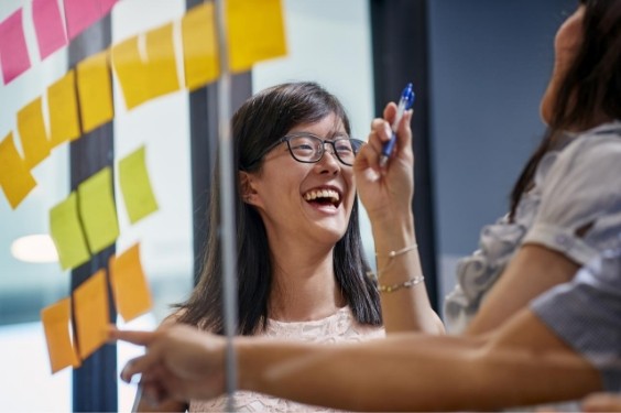 Coworkers laughing and smiling while they work around a noteboard.